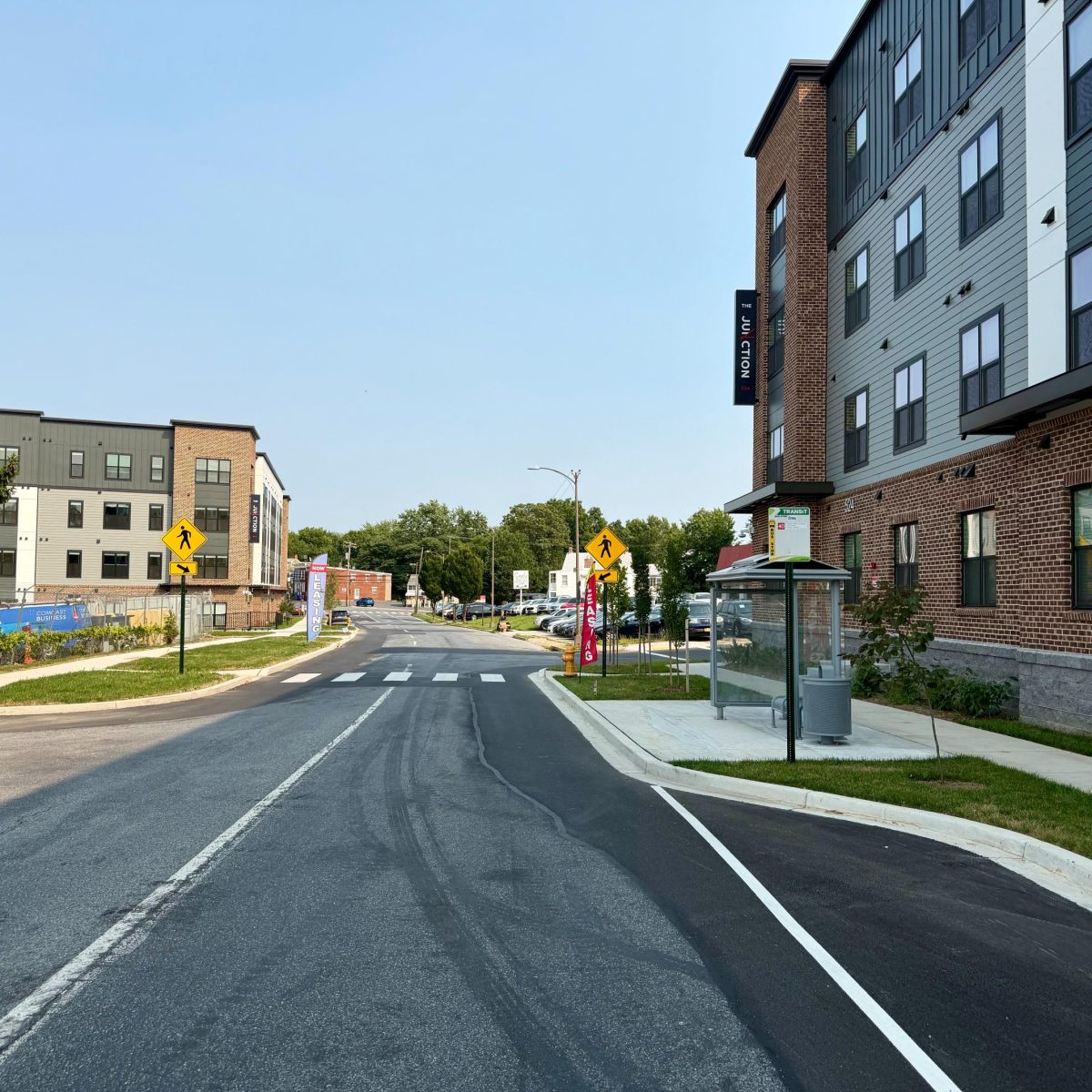 Street view of The Junction apartment buildings with crosswalks, a transit stop, and leasing banners in Frederick, MD