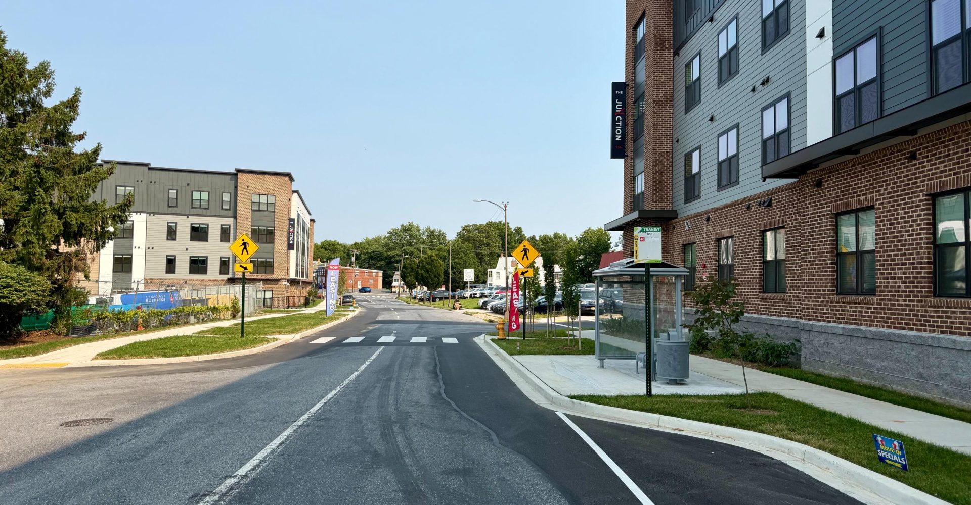 Street view of The Junction apartment buildings with crosswalks, a transit stop, and leasing banners in Frederick, MD