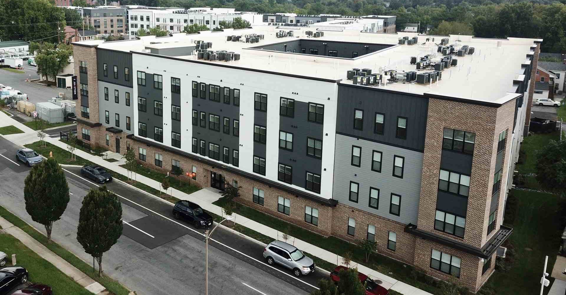 Aerial view of The Junction apartment building exterior with brick and gray siding along a tree-lined street in Frederick, MD